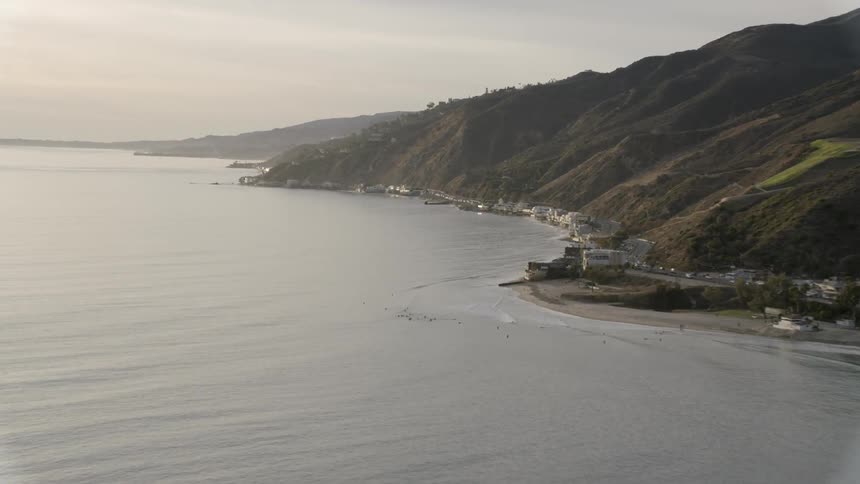 Cars travel on a road at the base of ocean front hills along the coast at sunset