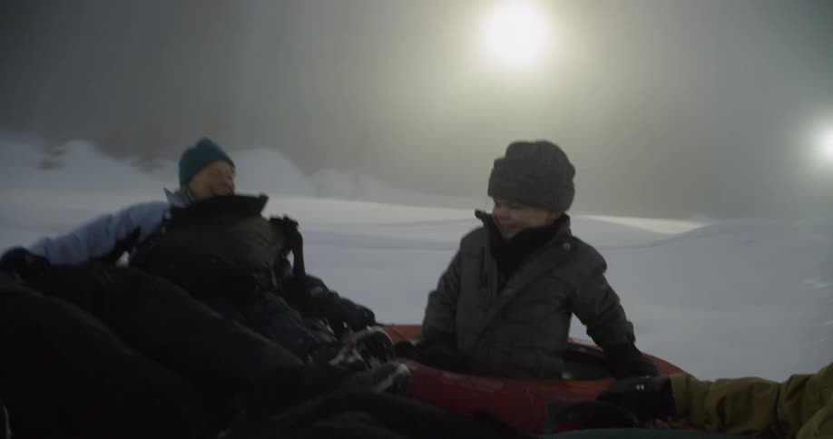 A family sleds down a hill in snow tubes