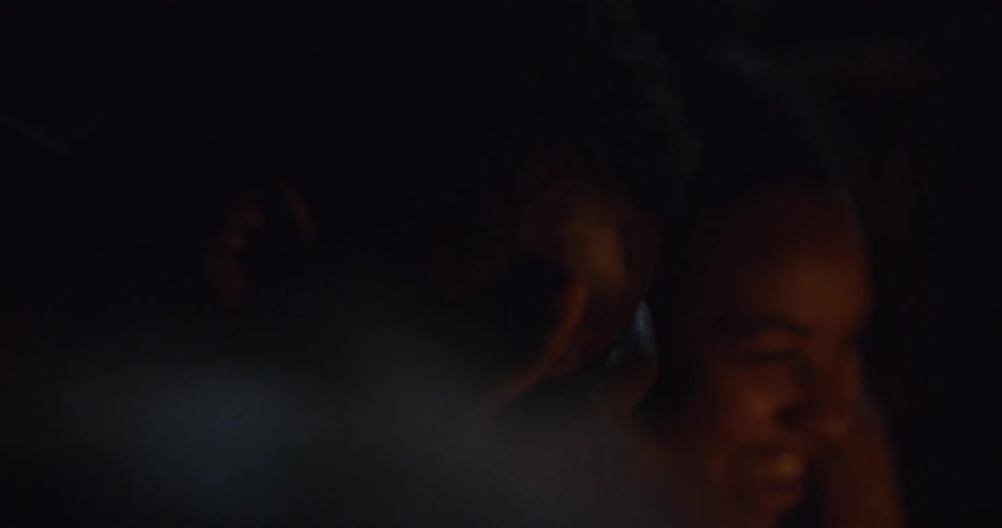 Black man and woman sit down in front of the campfire and laugh at night