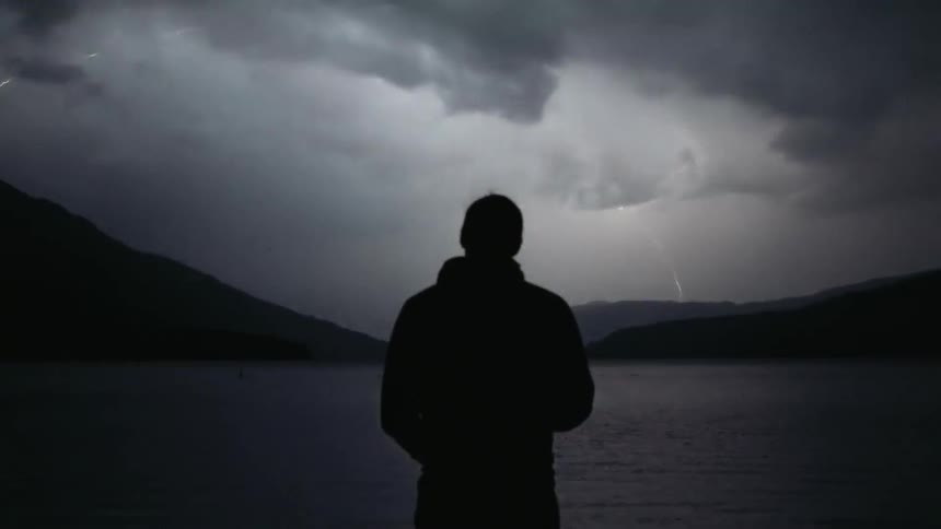 A man watches a lightning storm from the lake