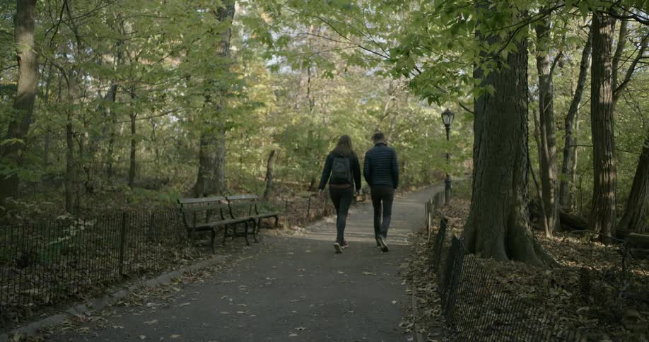 A young man and woman stroll down a path through a wooded park