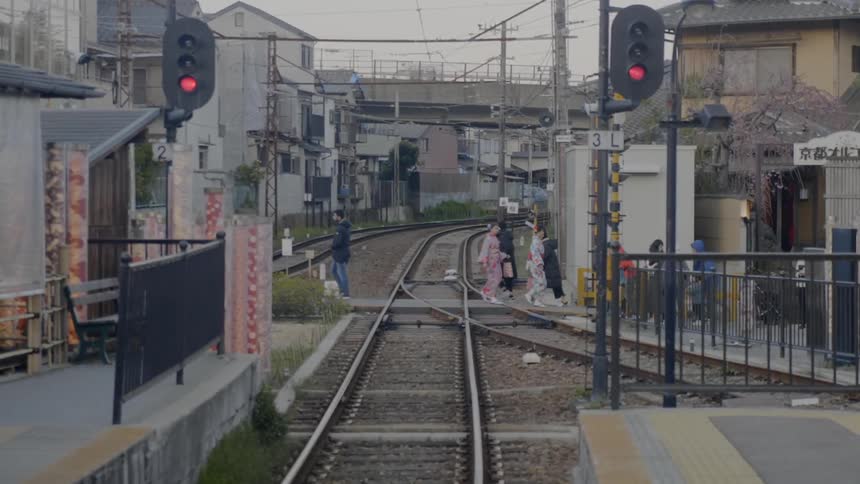 People walk on a sidewalk at a train station that crosses over train tracks