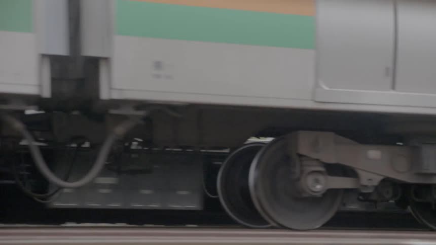 A train drives through a train station with people waiting to the side