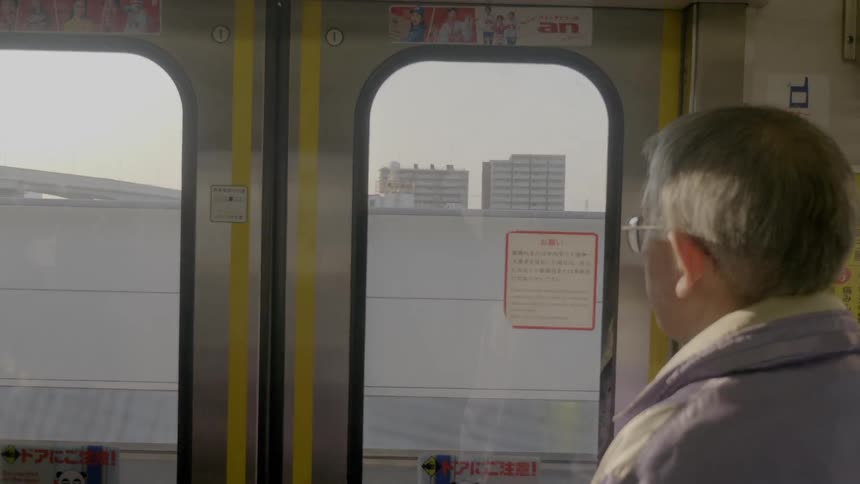 Elderly male stands watching out the window of a train as it moves along the rails above the city