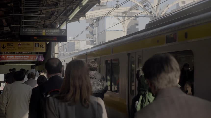 People walk in a train station as a train passes by