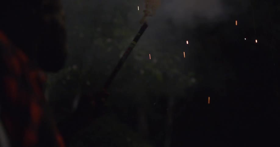 In the dark of night a person fires off small sparkling fireworks into the sky