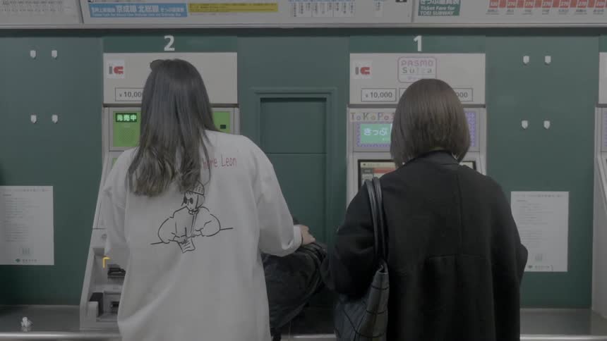 Woman in white sweater using an atm as another woman in dark coat approaches to use an atm next to her