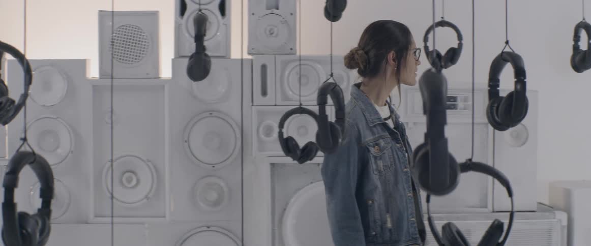 Headphones suspended from the ceiling by string as a woman looks at them with wonder