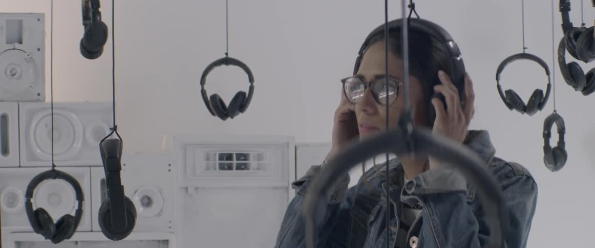 A woman sees several headphones hanging from the ceiling and tries on a pair