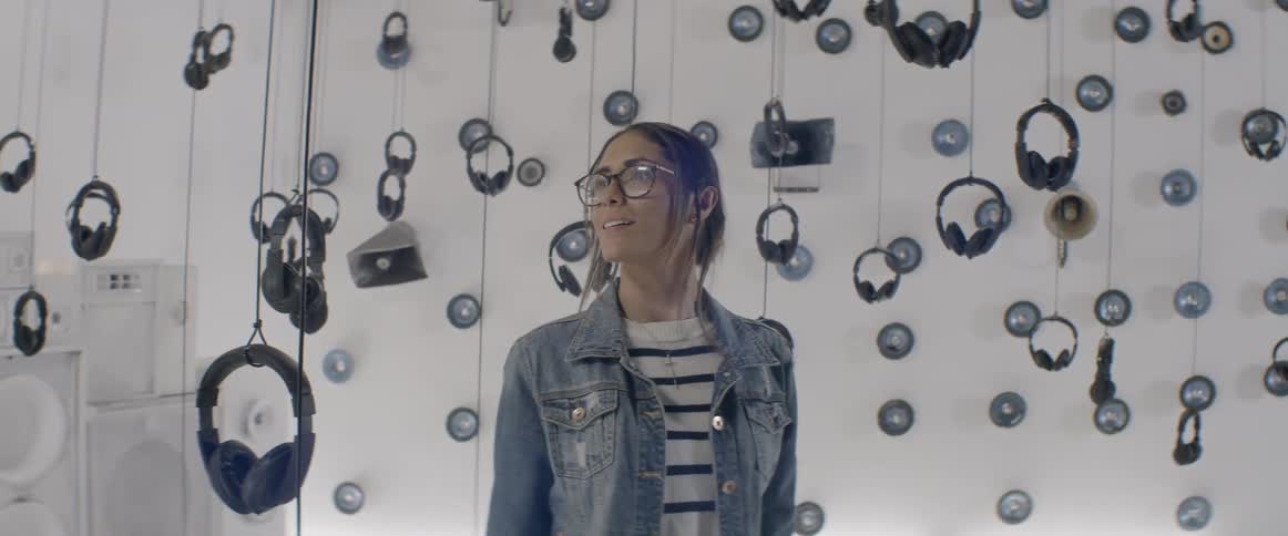 Headphones suspended from the ceiling by string as a woman looks at them with wonder