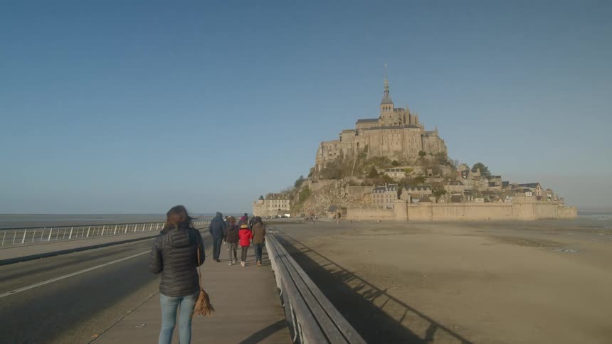 A woman in a coat stands staring at mont saint michel
