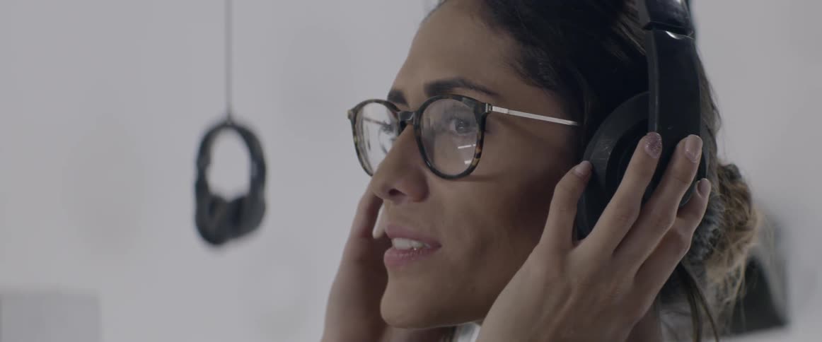 A woman wearing glasses is wearing headphones and turning her head