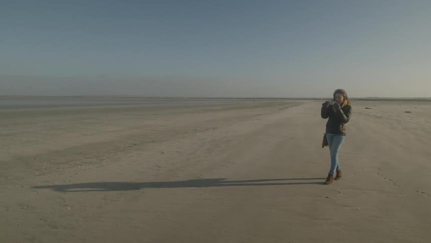 A woman taking a photo on a beach in normandy