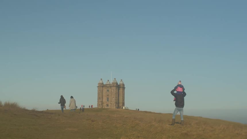 People walking in the fields around a castle