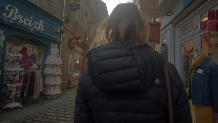 A woman is walking down a street past several clothing shops