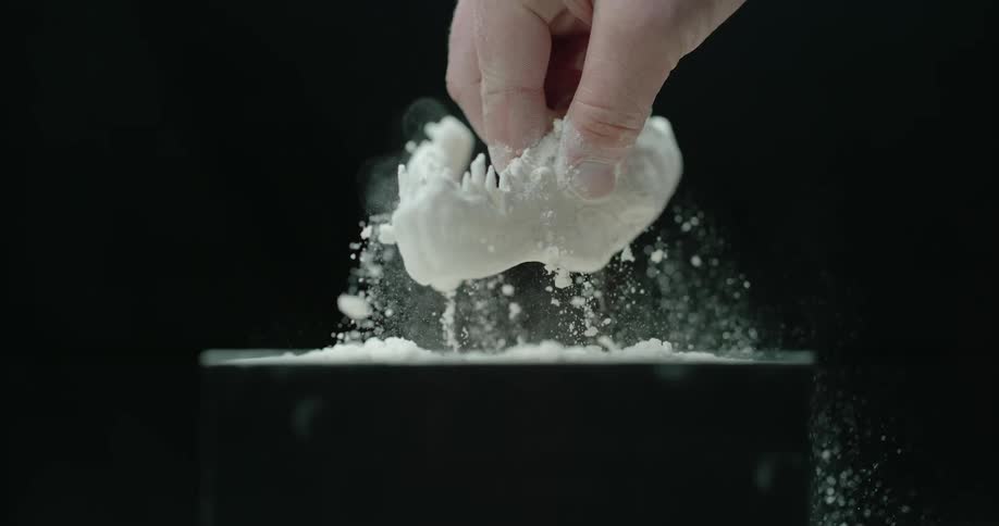 Fingers pull a small animal jawbone out of a container with white powder and then shake it off