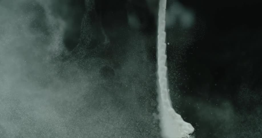 A strip of mesh material hangs in a darkened place and has a large amount of white powder shaken from it
