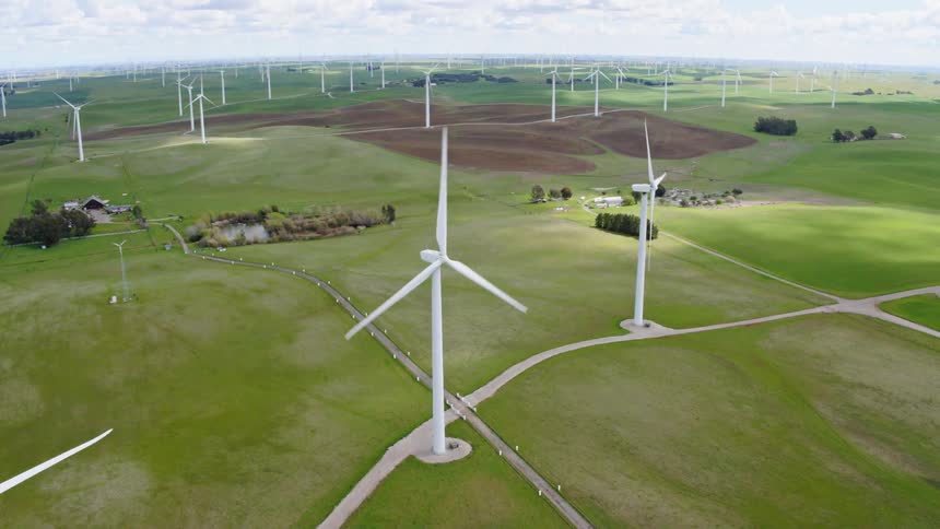 A windmill farm covering a large area of land dotted with buildings and roads