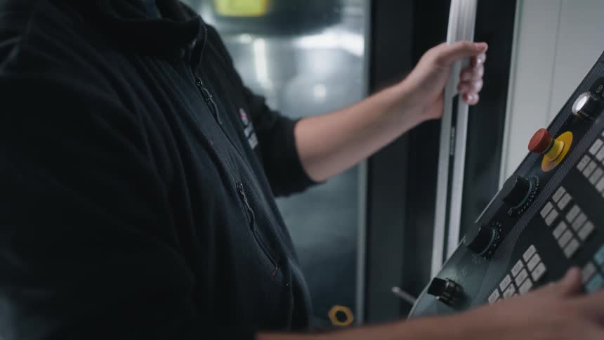 A worker turns dials and holds a lever on a control board