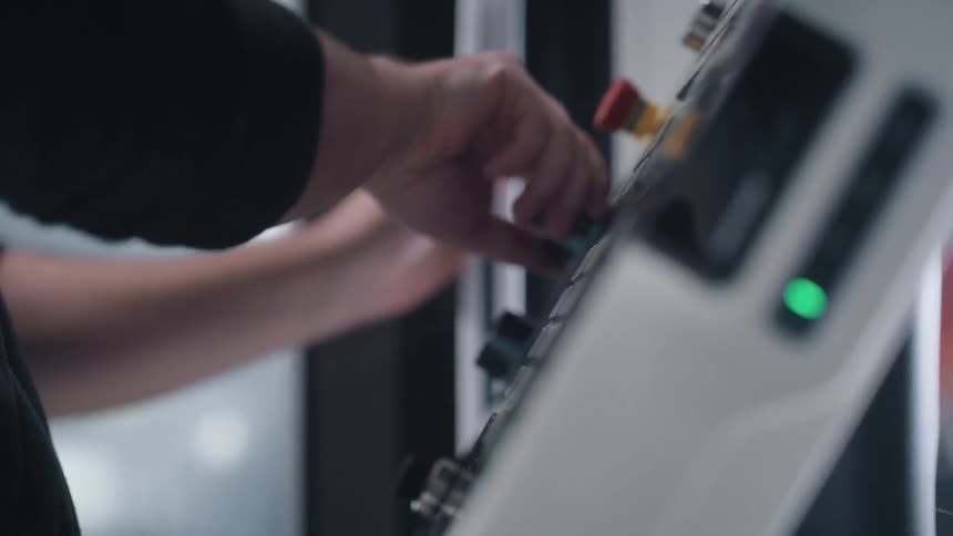 A man pushes buttons and turns knobs on a large control panel