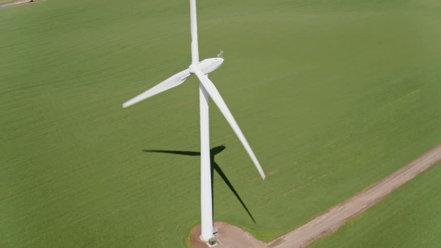 A wind turbine standing in a grassy field turns in the breeze