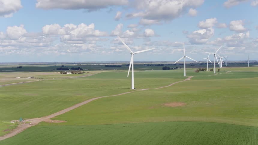 A row of spinning wind turbines are placed in a wide open grassy plane