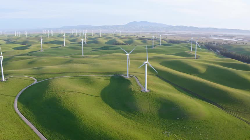 Several wind turbines are turning in a wind turbine farm with green grass