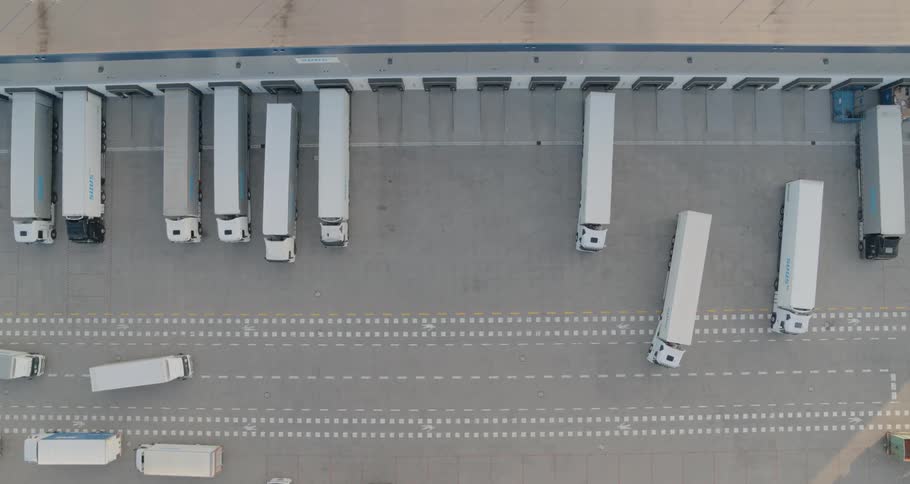 Multiple tractor trailers drive in the parking lot of a warehouse