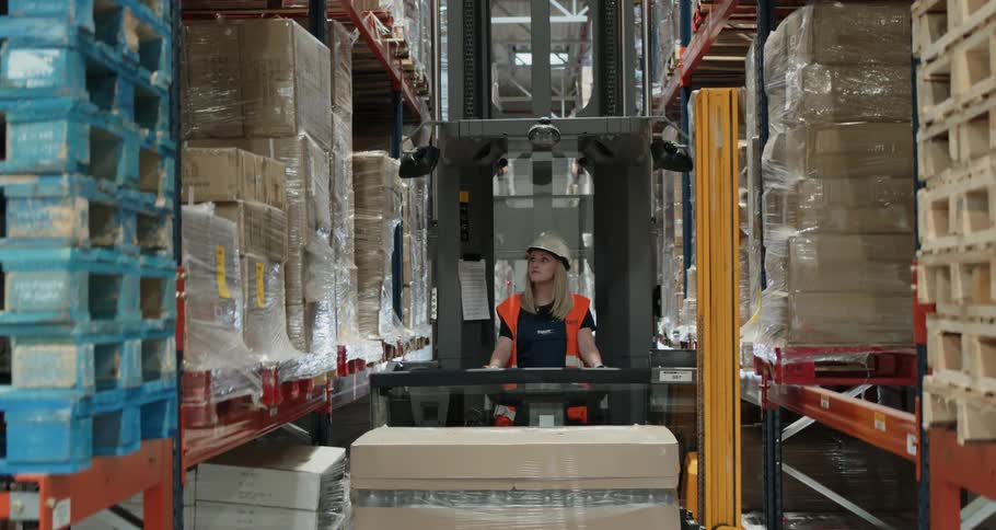A woman uses a forklift to raise pallets in a warehouse
