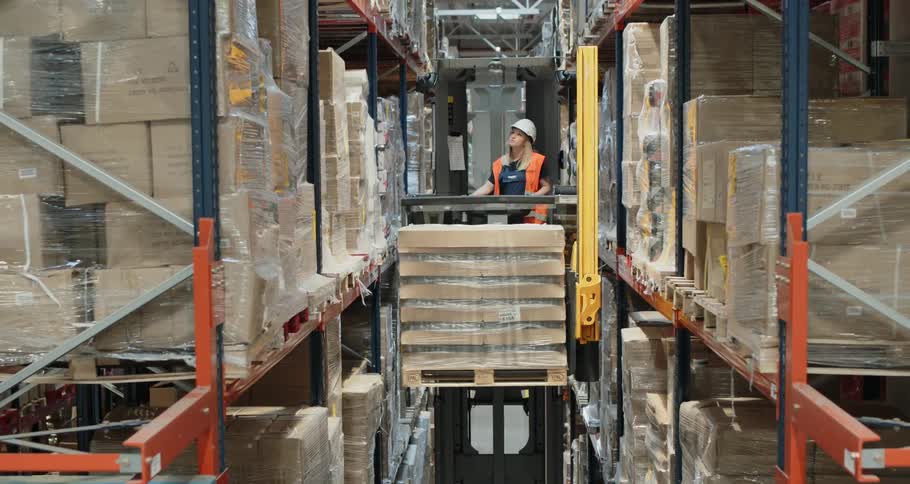 A woman operates and elevates a specialized lift to place a pallet of supplies on a high shelf