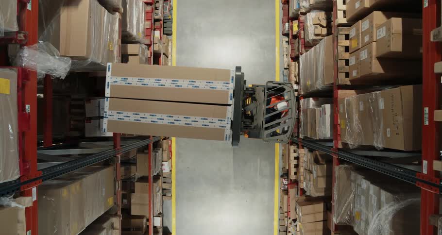 A forklift maneuvers and elevates to place boxes on a high shelf in a warehouse