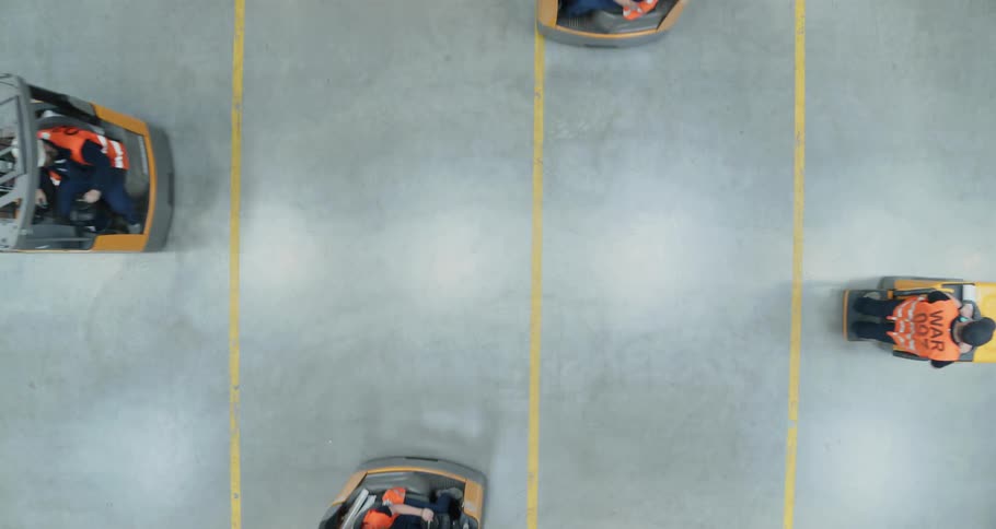 A group of people ride forklifts in all different directions in a warehouse