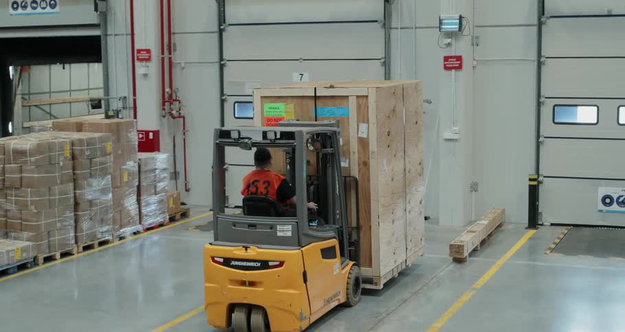 A man with an orange vest driving a forklift in a warehouse