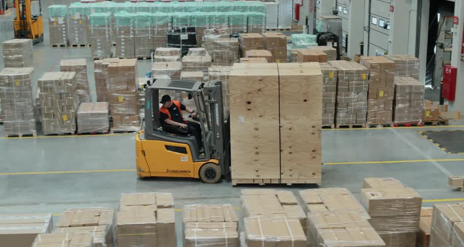 A man drives a full forklift backwards in a warehouse