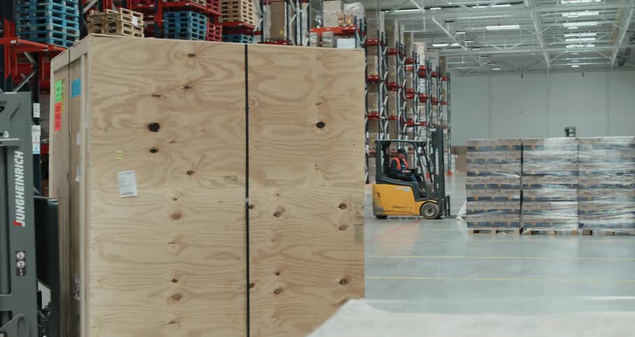 A man drives a full forklift into a trailer in a warehouse