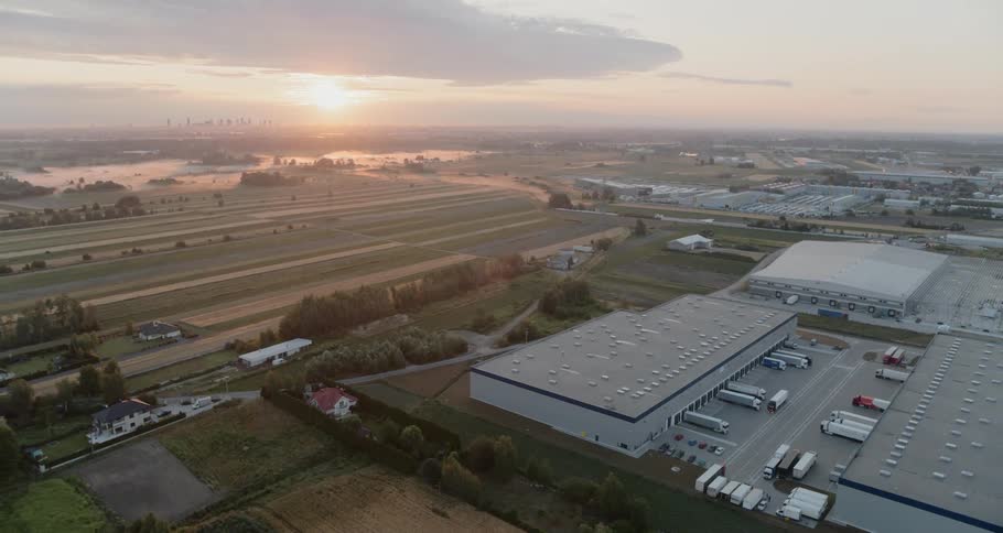 Several trucks are parked next to some warehouses as the sun sets