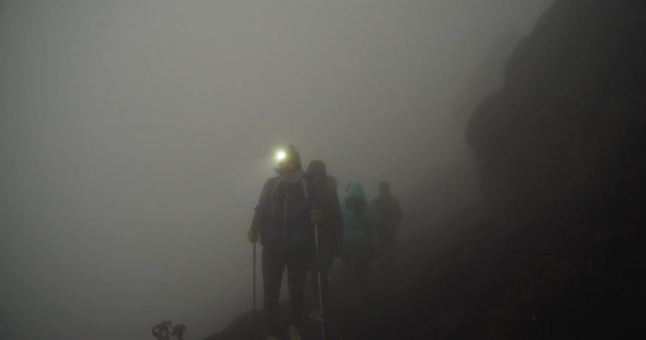 Line of hikers move carefully along fog shrouded mountain trail