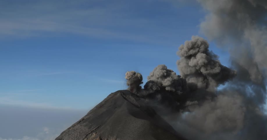 Black smoke rise from mountain top against clouded blue sky
