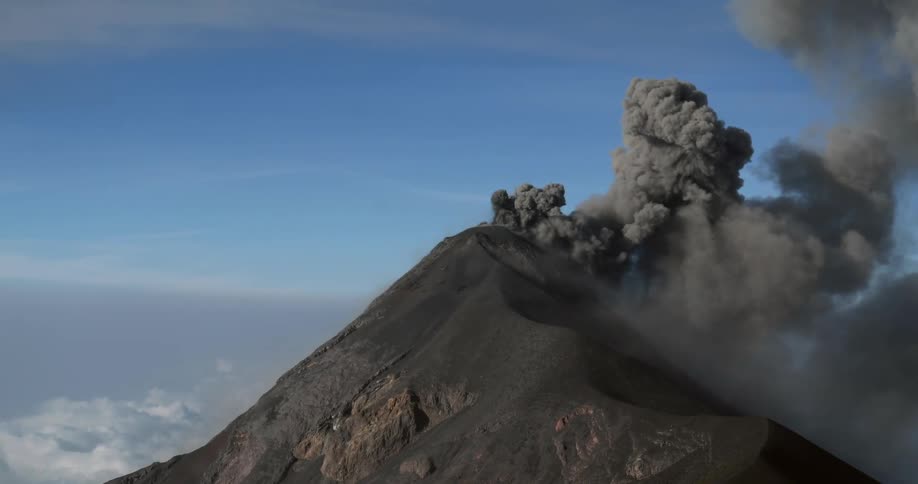 Black smoke billowing from a volcano covered in ash