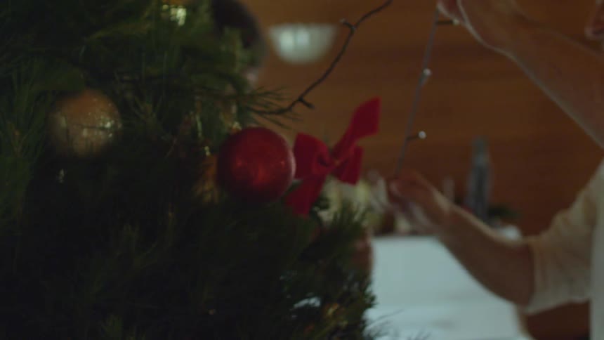 A man in a white shirt arranges lights on a christmas tree