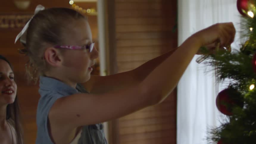 A girl hangs a gold ribbon on a christmas tree