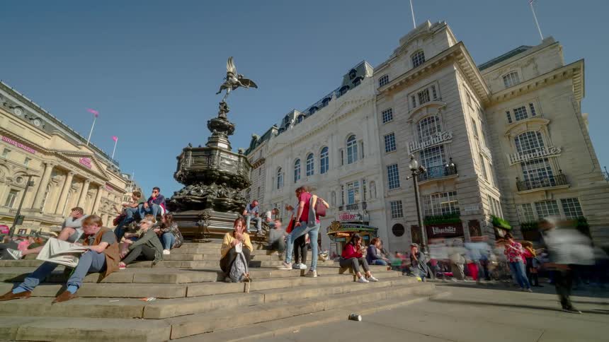 Tourists sit on the steps of the shaftesbury memorial fountain and take pictures in london