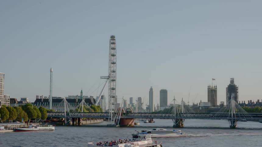 A ferris wheel spins next to a river that is traversed by numerous boats