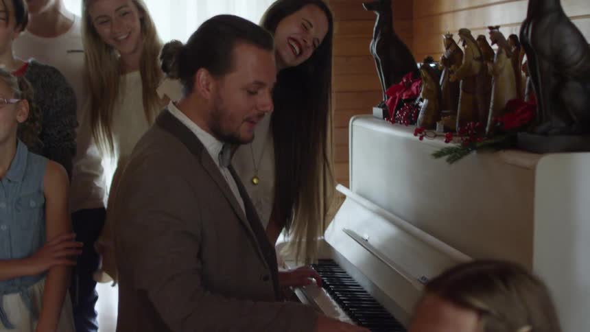 People gathered and singing around a man who is singing and playing the piano
