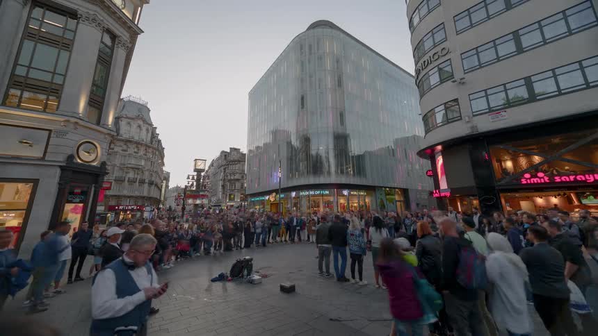 A large crowd is gathered around in a downtown area to watch a street performance