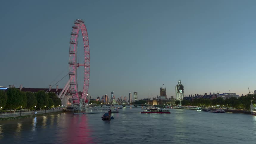 Watercraft travels on the river as a ferris wheel sits nearby