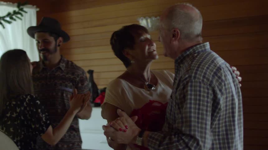 Two couples dancing in a home in front of a fireplace that is decorated for the holidays