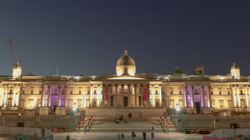 A large white building with pillars and steps in front where people sit