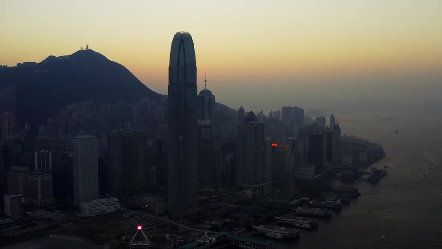 Downtown skyscrapers stand between mountains and ocean with orange sky