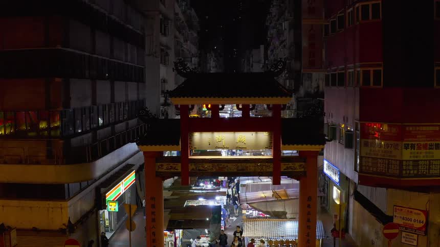 Beyond a chinese style archway a city street is completely lined with numerous canopies under which vendors sell their wares
